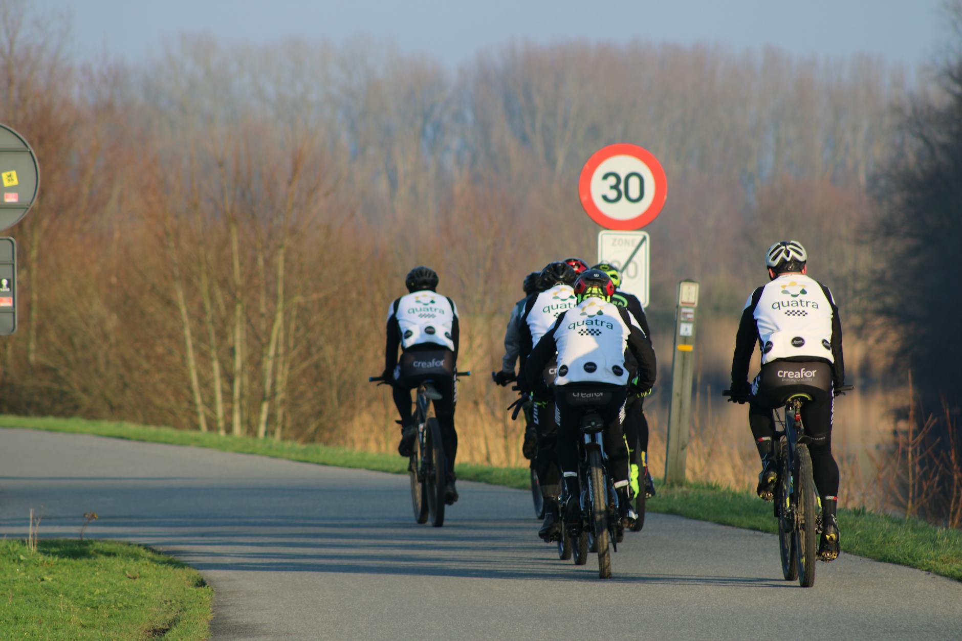 Grupa rowerzystów jedzie wiejską drogą w Belgii obok znaku ograniczenia prędkośc