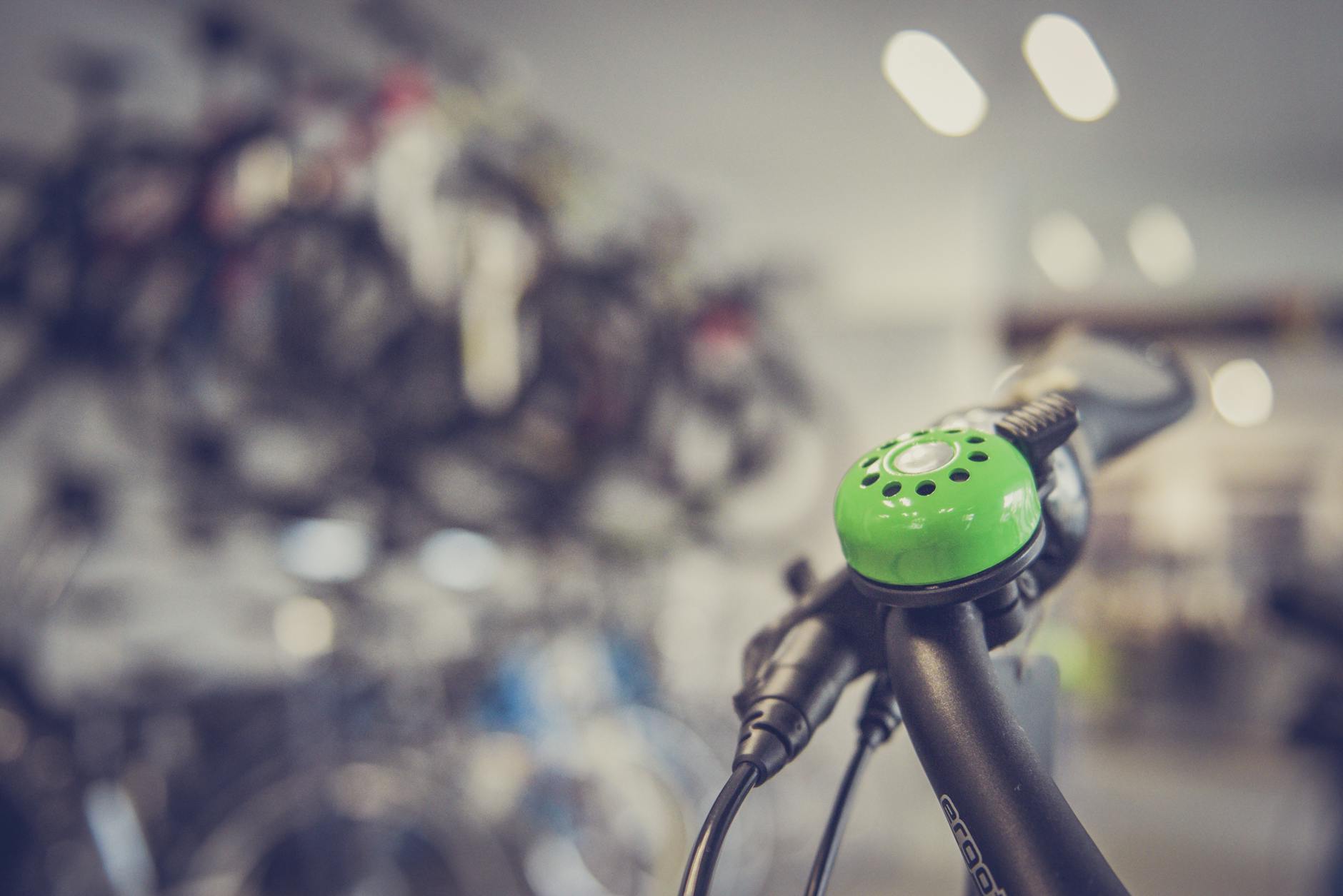 Zielony dzwonek na kierownicy roweru na tle wnętrza sklepu rowerowego