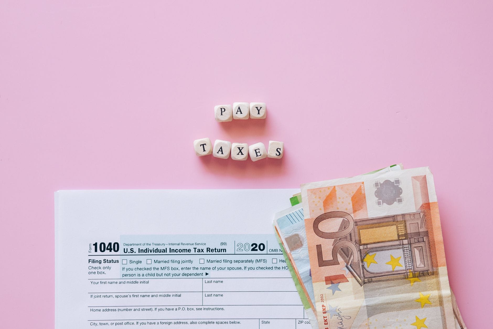Formularz podatkowy z banknotami euro i napis pay taxes na różowym tle