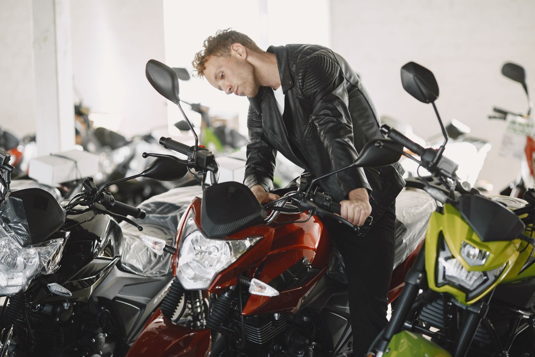 Mężczyzna w skórzanej kurtce ogląda motocykle w salonie dealerskim